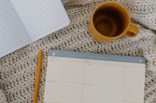 Un planning hebdomadaire posé sur une table, à côté d’un carnet et d’une tasse de café : la séance de préparation de 30 minutes