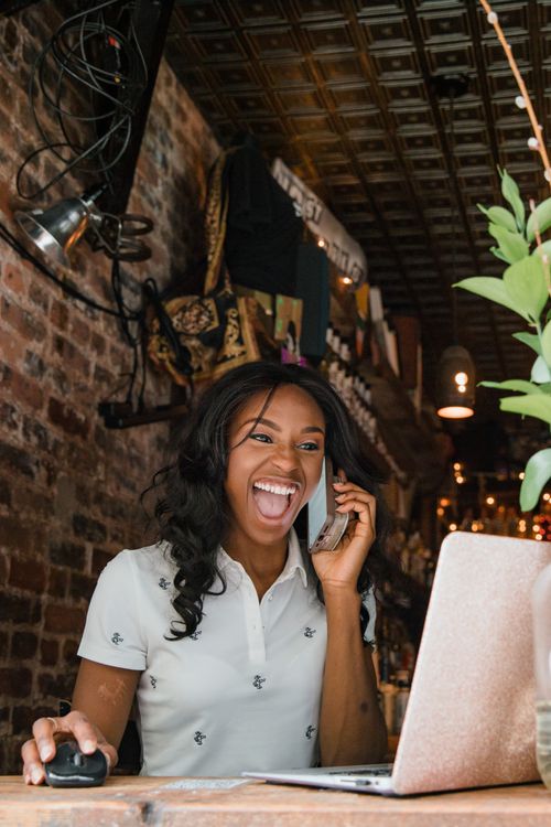 Une commerçante souriante au téléphone devant son ordinateur, dans sa boutique